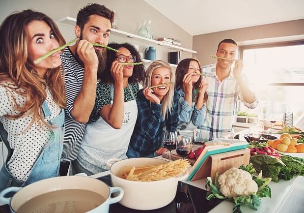 Group of chefs playing with asparagus stalks while standing in front of bowls of water, pasta and vegetables